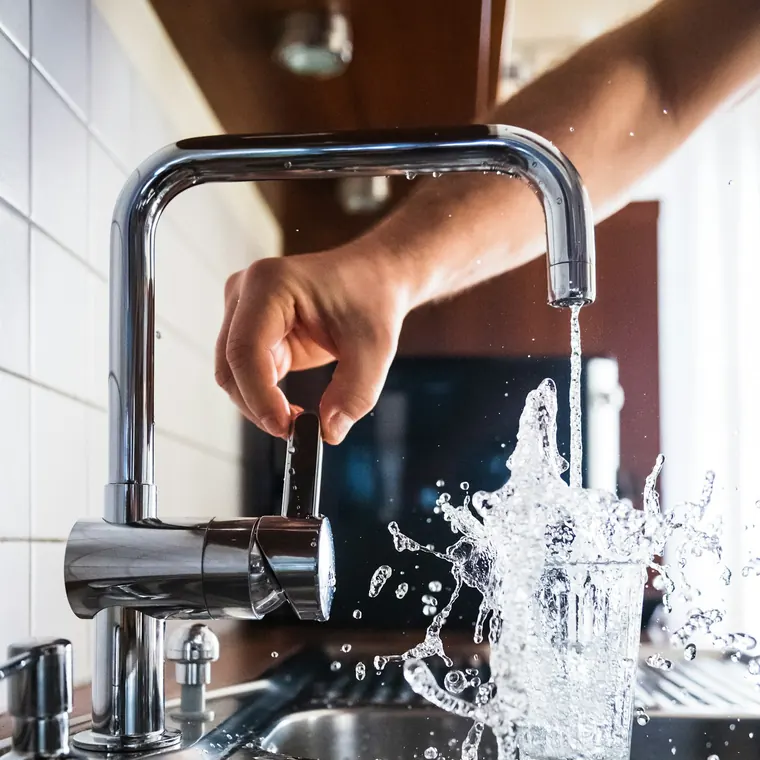 Mano abriendo una llave monomando sobre un lavaplatos con agua corriendo